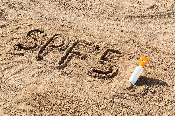 防晒系数五。SPF 5字写在沙子上，白色的瓶子上涂有防晒霜。皮肤护理概念背景。