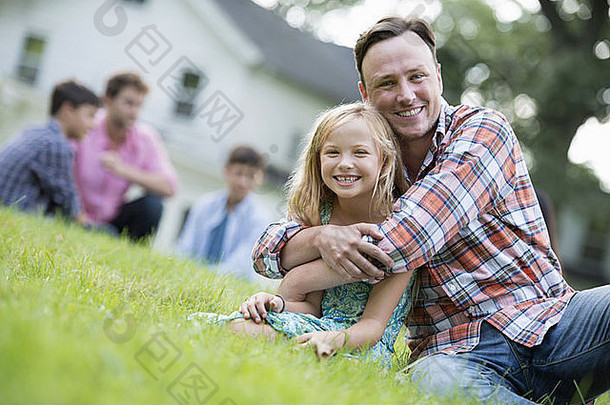 一对父女坐在草地上参加夏季聚会。