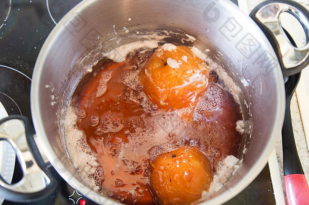 俯视图：木瓜在糖浆中，在一个<strong>不锈钢</strong>大锅中慢炖。水果中的单宁使它们变成了<strong>红</strong>宝石色。