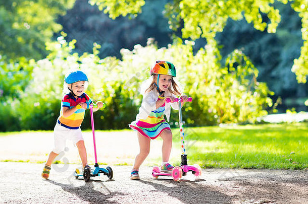 在阳光明媚的夏日，孩子们在公园里<strong>学习</strong>骑滑板车。戴着安全帽的学龄前男孩和女孩骑着压路机。孩子们在户外玩滑板车