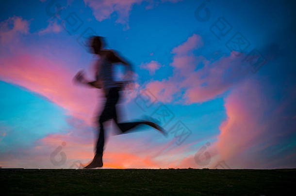 五颜六色的日落图，一个男人的轮廓在运动模糊中奔跑。放慢快门速度，增强运动感。