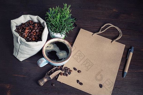 咖啡的静物画。牛皮纸袋、咖啡杯、咖啡豆、植物和复古木桌子背景上的钢笔。
