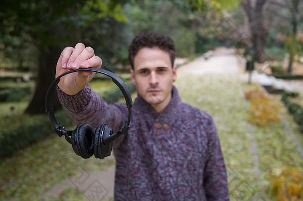 在秋天公园里，一个年轻人拿着并展示着耳机看着摄像机。