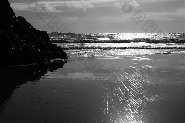 英国康沃尔郡凯南斯湾，深色岩石反射在潮湿的沙滩上，海浪进入海滩