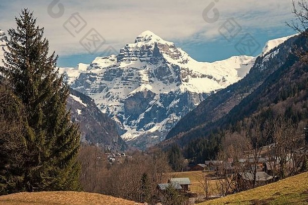 法国阿尔卑斯山脉美丽的阿尔卑斯山风景。一座雪山矗立在绿树成荫的山谷和风景如画的山村后面。