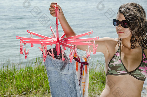 在康斯坦斯湖畔，一位穿着比基尼的迷人年轻女子手持一台小型旋转式干衣机，上面挂着干毛巾