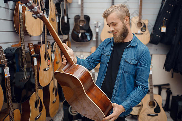 留胡子的年轻人在音乐商店挑选吉他