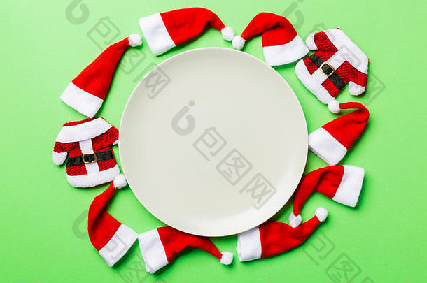 节日用的一套盘子，在五颜六色的背景上装饰着圣诞老人的帽子。俯视圣诞晚餐概念。