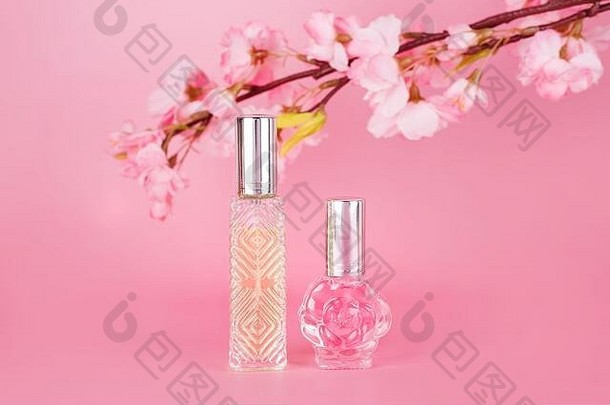 不同的透明香水瓶，粉色背景上有春天盛开的树枝。樱花春花芳香香精瓶