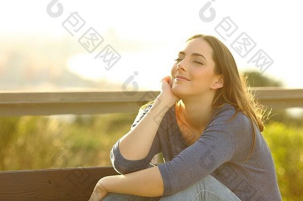 在城市郊区的户外日落时分，一位心满意足的女士坐在长椅上休息