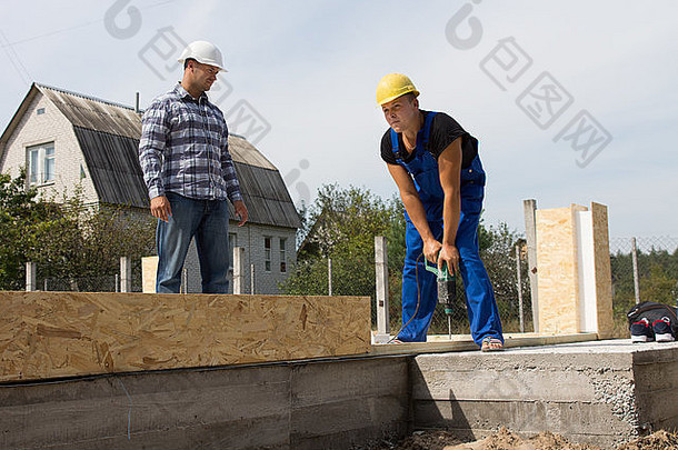 男建筑工程师看着建筑工人忙着在工地上钻木头。