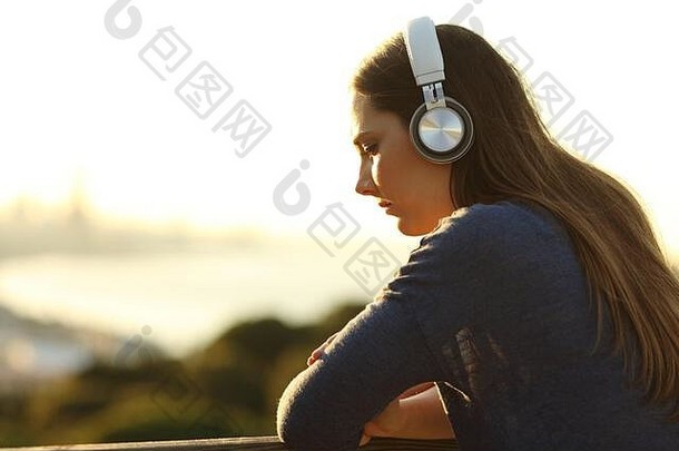 悲伤忧郁的女人在日落时听着音乐，在阳台上俯视