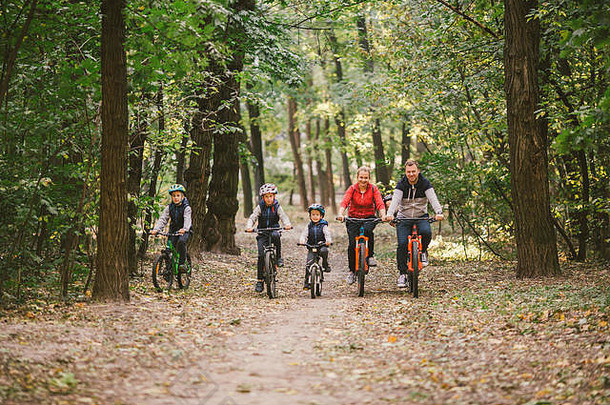 父母和孩子在森林小道上骑自行车。年轻的家庭在秋季公园骑自行车。一家人在森林里骑山地自行车。主题家庭户外<strong>运动</strong>