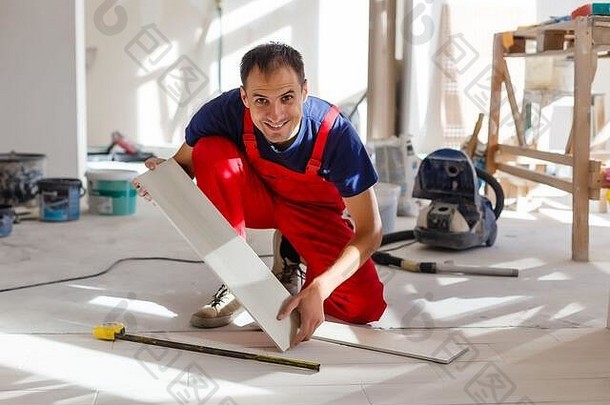 主人穿着工作服，正在检查瓷砖的地平线，使用建筑标高，调整，专业维修工作