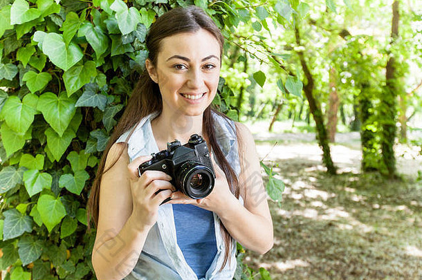 公园里带着复古相机微笑的年轻女业余摄影师的肖像