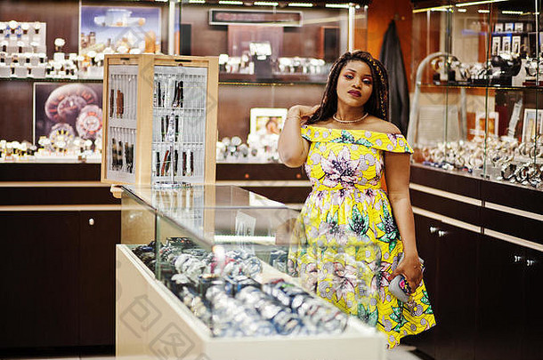 可爱的身材矮小的非洲裔美国女孩，留着可怕的长发，在购物中心的手表店里穿黄色的衣服。