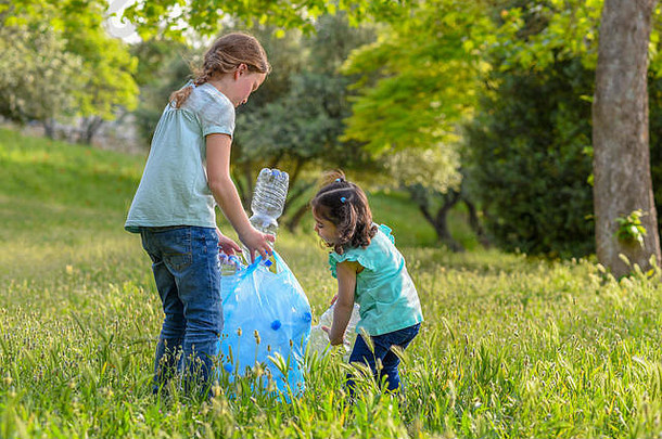 小女孩从草地上拿走塑料瓶。孩子们在公园里捡垃圾。