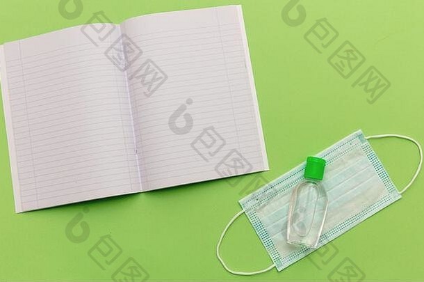 打开淡绿色背景上的空白学校笔记本、医用防护面罩和洗手液凝胶，俯视图、返校、冠状病毒日。透射电镜