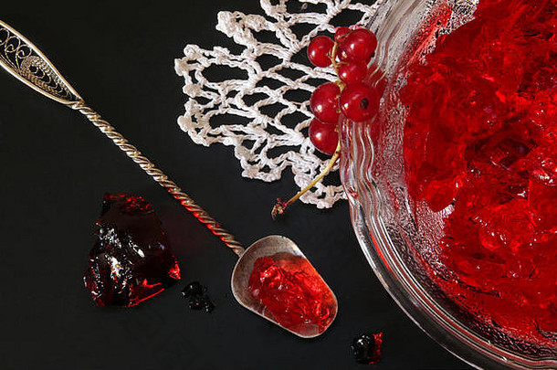 黑底玻璃碗中的红醋栗果冻。花边餐巾和漂亮的甜点勺