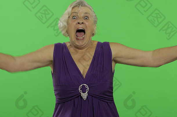 一位老妇人露出惊讶、喜悦和微笑。穿着紫色连衣裙的快乐的老奶奶。放置您的徽标或文字。色度键。绿色屏幕背景