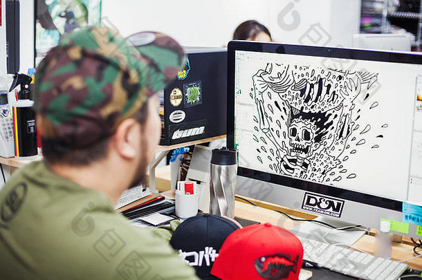 设计工作室。一名男子坐在办公桌前，用电脑设计T恤图案。