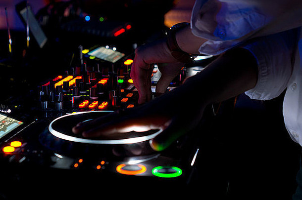 夜晚，色彩鲜艳的DJ音乐台上所有的控制装置都亮起，唱片骑师的手悬挂在转盘上的乙烯基唱片上方，为迪斯科舞厅混音和刮音。