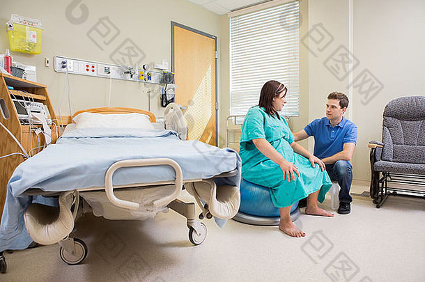 男子在医院里看着健身球上的怀孕妻子