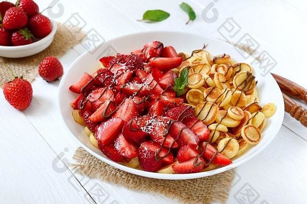 在一个碗里煎饼麦片，在白色木质背景上放上新鲜草莓和坚果。美味时尚的早餐。有机荷兰迷你煎饼。