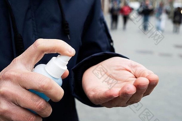 一个白人男子在街上用瓶子里的蓝色洗手液洗手的特写镜头
