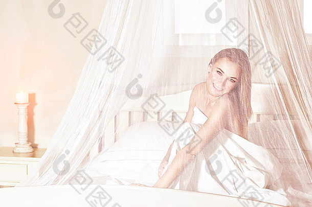 浪漫的女人坐在床上，在柔和透明的帷幔下，在豪华温泉酒店度过周末，享受休息