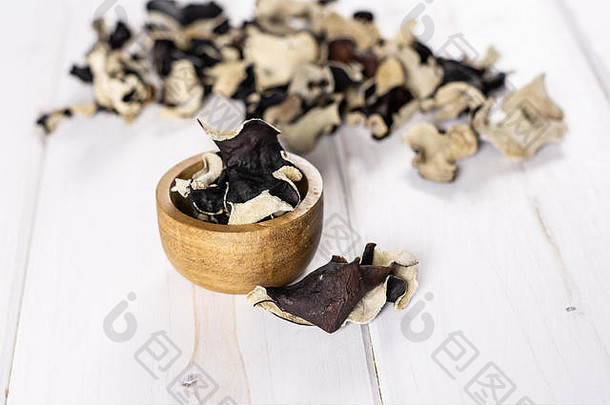 大量干黑蘑菇犹太耳片，白色木材上有木碗