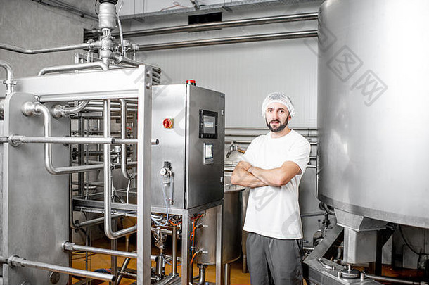 一位英俊的工人在奶酪或牛奶厂使用控制面板操作巴氏杀菌机的肖像