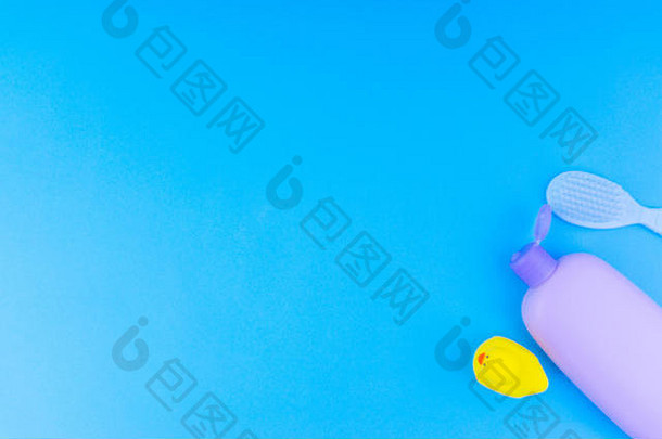 蓝色背景上模糊的婴儿护理产品平面构成。从上面看洗发水或淋浴瓶凝胶、清洁刷和黄色橡胶