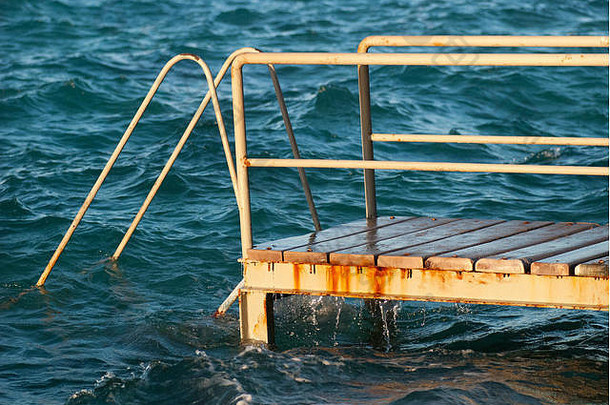古老的老式金属木楼梯从海滩通向蓝绿色海水。美丽的夏日。海边的游泳池，配有格伦格复<strong>古楼</strong>梯。侧视图
