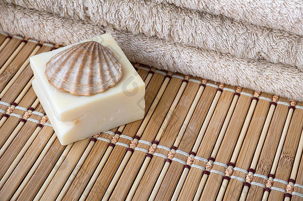 天然牛奶皂条、扇贝壳和毛圈毛巾放在竹垫上
