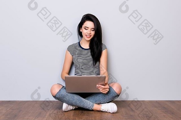 穿着休闲服的快乐年轻女子坐在地板上，一边用笔记本电脑工作，一边登记