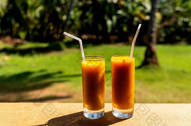 在热带花园的背景上，两杯鲜榨芒果汁。