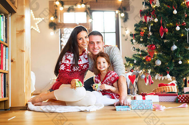 一个年轻的家庭和女儿在家里的圣诞<strong>树</strong>旁。