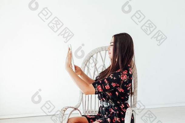 漂亮时尚的黑发女人坐在椅子上，手里拿着一个互联网平板电脑