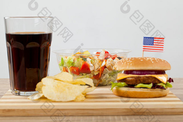 美味的芝士汉堡配牛肉、切达干酪和生菜，一面薯片和一杯可口可乐饮料放在木板上