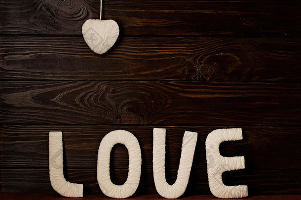 情人节的概念。字母“爱”和“心”由深色木质背景上的纱线制成。