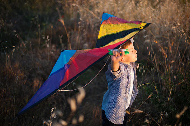 快乐、健康、可爱、<strong>有梦想</strong>的小孩，肩后扛着玩具彩色风筝，站在干草中间，在温暖的日落中想着飞行