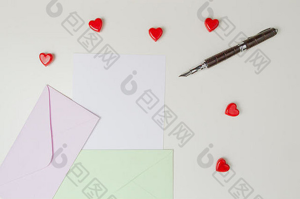 信封、短信、钢笔和白色桌子上的红色小红心。情书、情人节概念