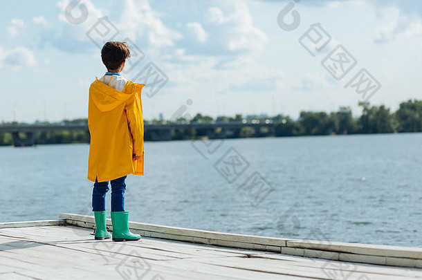 黑头发的男孩穿黄色的雨衣高统靴