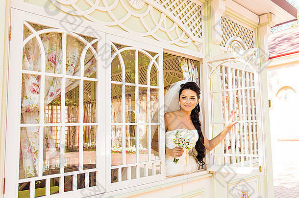 年轻美丽的新娘在窗前等待新郎。美丽的新娘被阳光照亮。美丽的年轻新娘在等待