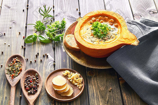 用姜和大蒜调味的辛辣南瓜汤，在镂空的南瓜中加入面包片、欧芹和奶油。秋天的食物背景，文字空间。