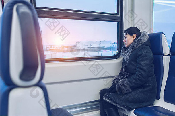 年轻漂亮的女孩坐在火车上，看着窗外冬日的日落