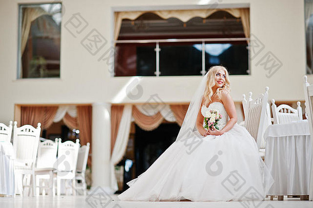优雅的金发碧眼时尚新娘坐在婚礼大厅的椅子上