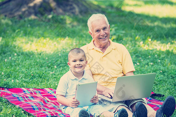快乐的老爷爷和孩子在公园里使用笔记本电脑