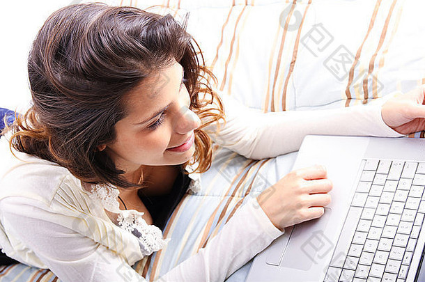 一个年轻女孩躺在床上，用笔记本电脑<strong>上网</strong>。